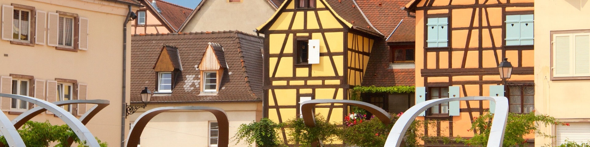 A European town with traditional half-timbered houses, a gate with a sign, and a flower bed.
