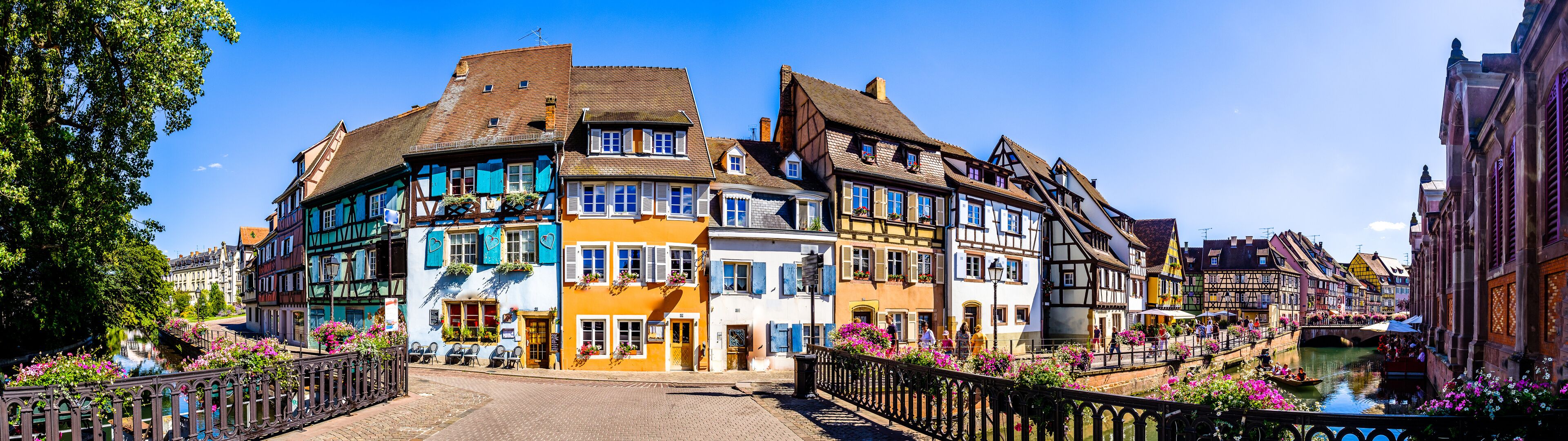 A picturesque European town with colorful half-timbered houses, a canal, and blooming flowers.