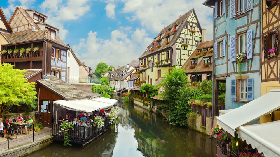 A narrow waterway flanked by traditional half-timbered buildings with balconies and flower boxes.