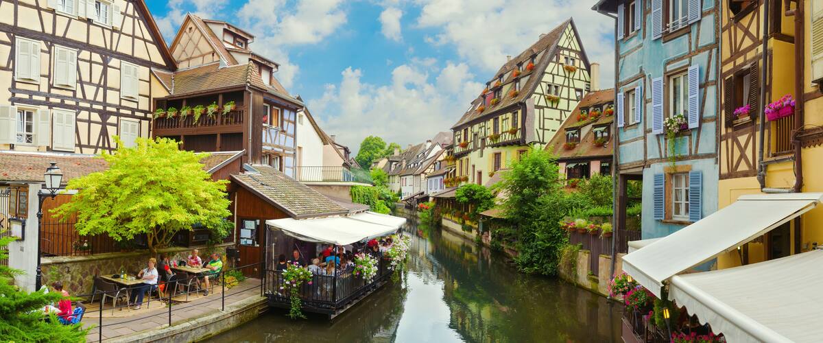A narrow waterway flanked by traditional half-timbered buildings with balconies and flower boxes.