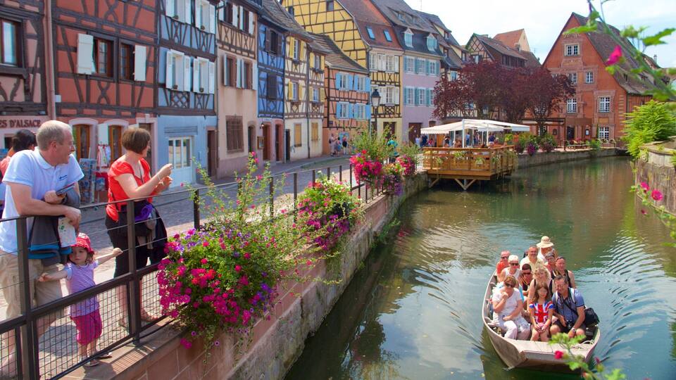 A canal with a boat tour, colorful buildings, and people along the walkway.