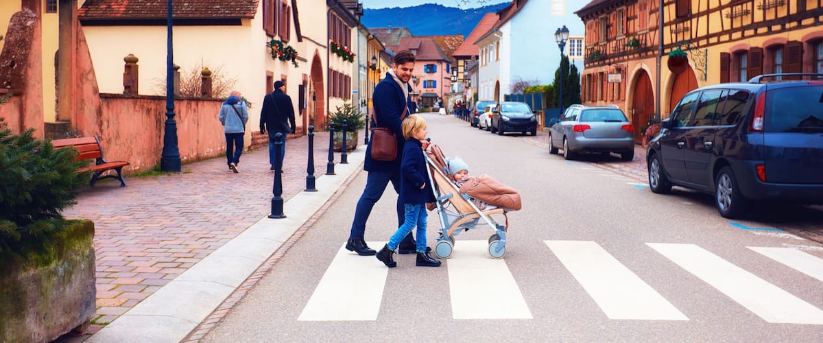 A cobblestone street with traditional European architecture, a pedestrian crossing, and parked cars.