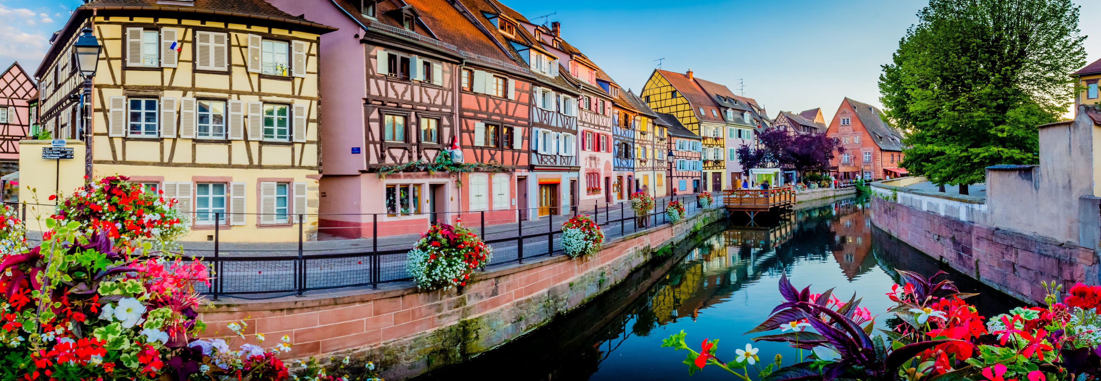 A canal with colorful half-timbered buildings on one side and a bridge in the distance.