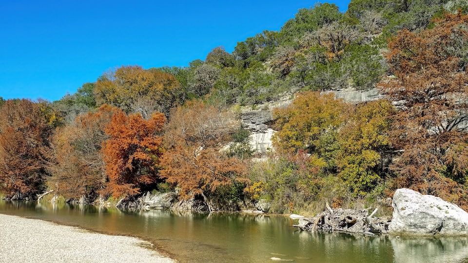 A river with clear water, surrounded by autumn-colored trees and rocky terrain.