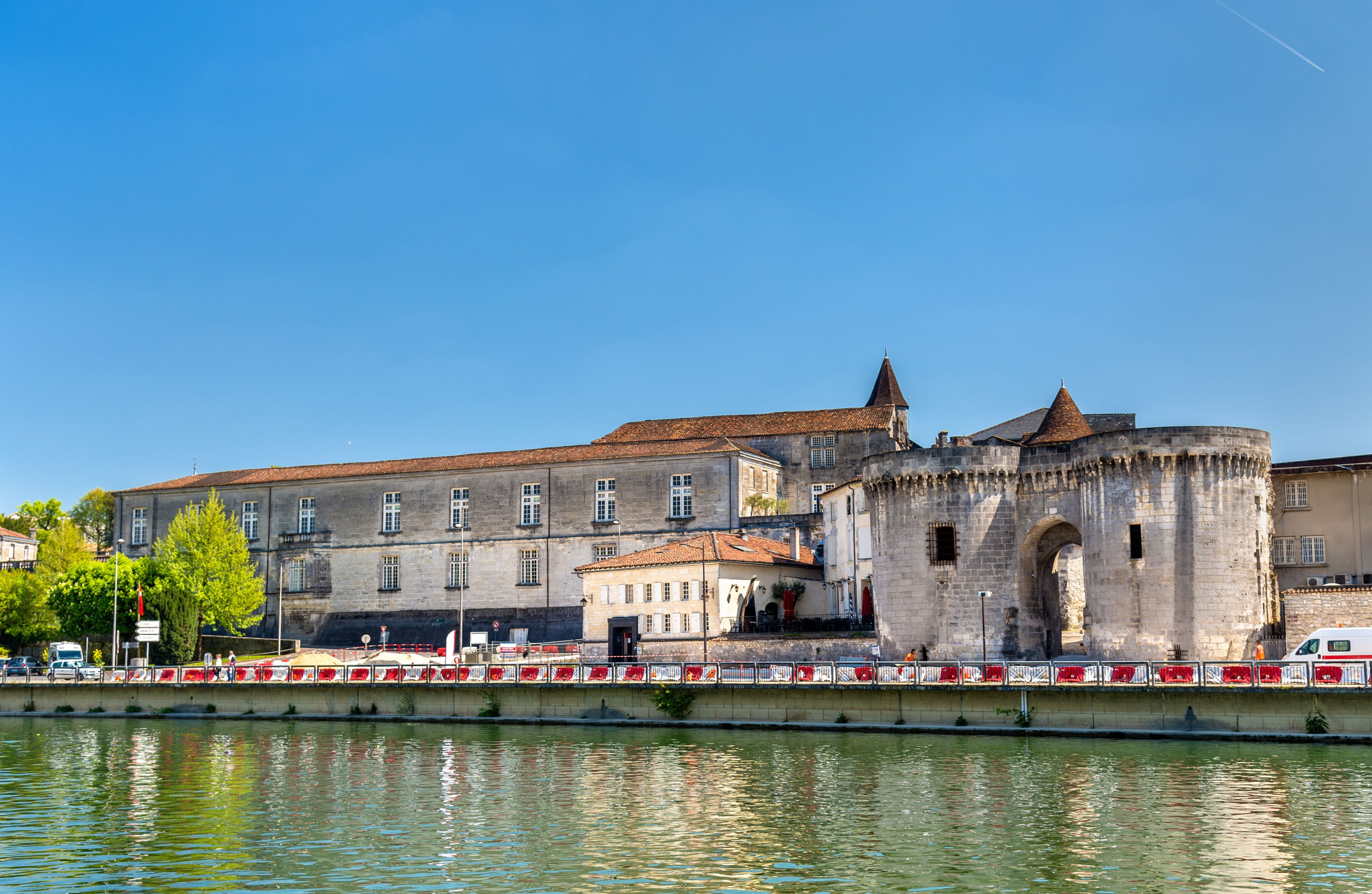 A historic building with a large arched entrance and a tower, situated by a calm river.
