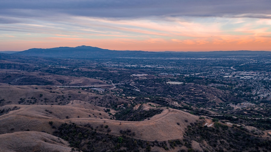 Aerial view of open rolling hills in suburban Southern California.  Radio tower atop hill during sunset surrounded by mountains and ocean