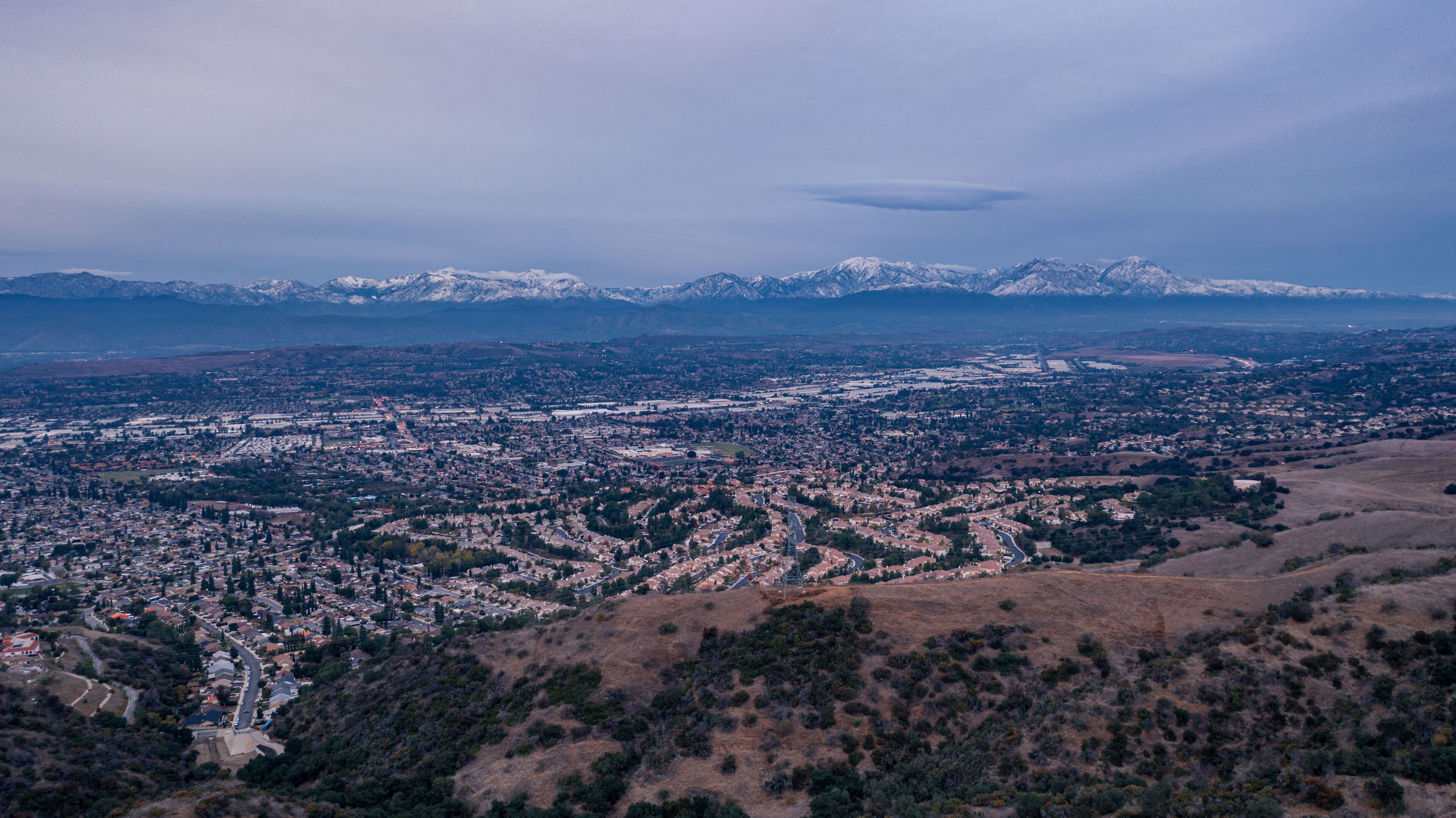 Aerial view of open rolling hills in suburban Southern California.  Radio tower atop hill during sunset surrounded by mountains and ocean