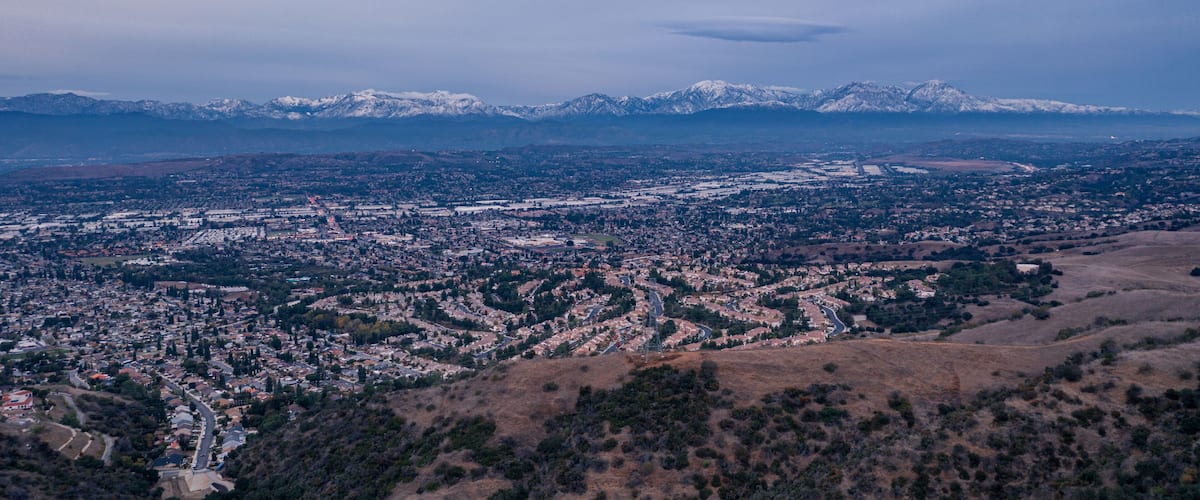 Aerial view of open rolling hills in suburban Southern California. Radio tower atop hill during sunset surrounded by mountains and ocean