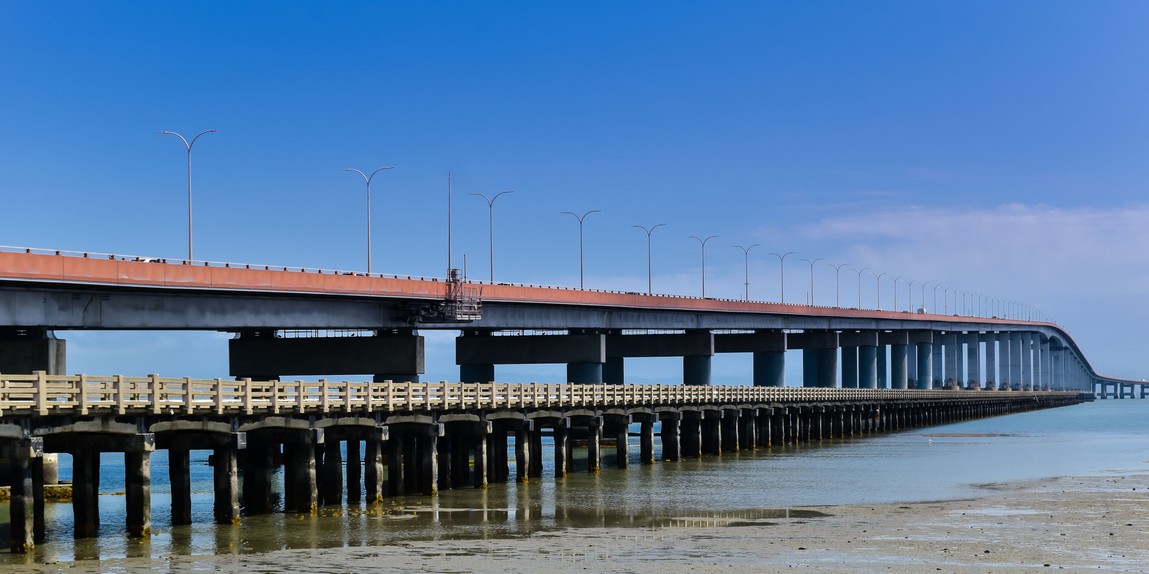A long bridge with a red roof and multiple streetlights extending over calm water.