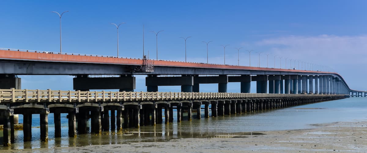 A long bridge with a red roof and multiple streetlights extending over calm water.