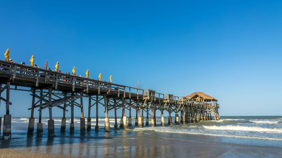 A pier extending into the ocean with a thatched-roof structure at the end.