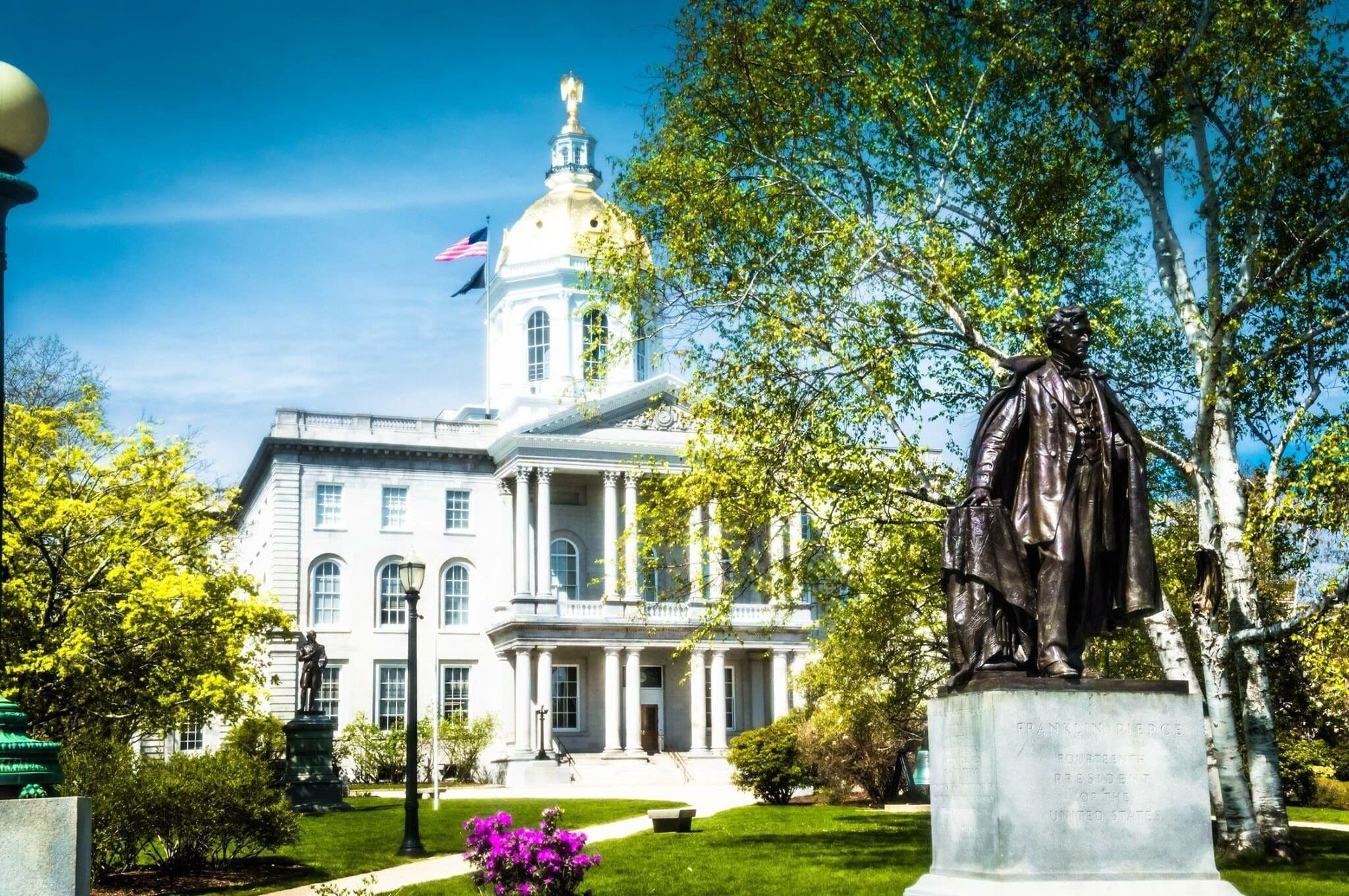A stately building with a prominent dome and columns, surrounded by lush greenery and a statue.