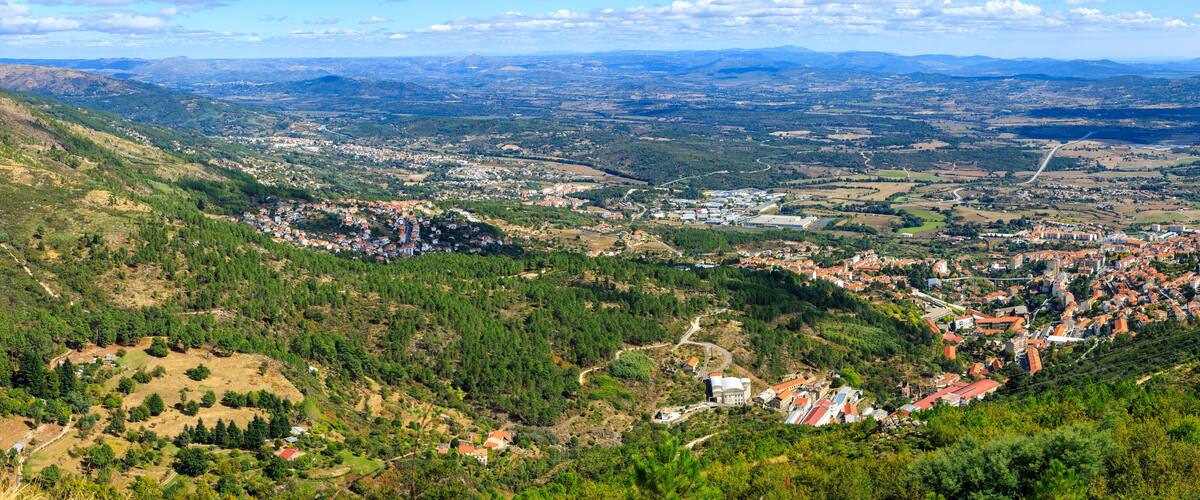 A mountainous landscape with a town nestled in a valley, surrounded by forests and fields.