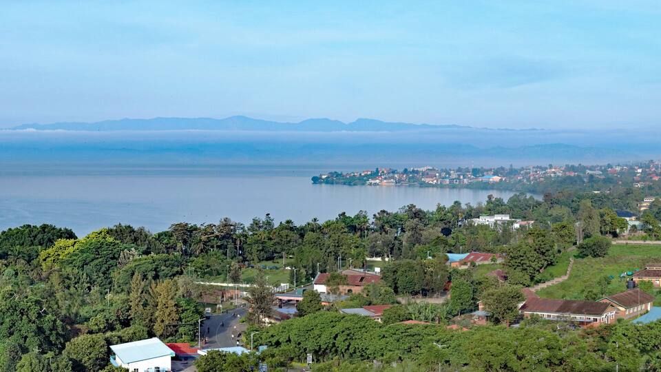 A coastal town with dense greenery, a large body of water, and distant mountains.