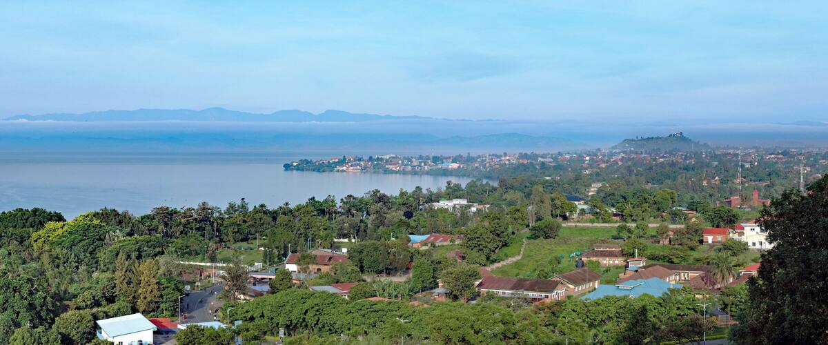 A coastal town with dense greenery, a large body of water, and distant mountains.