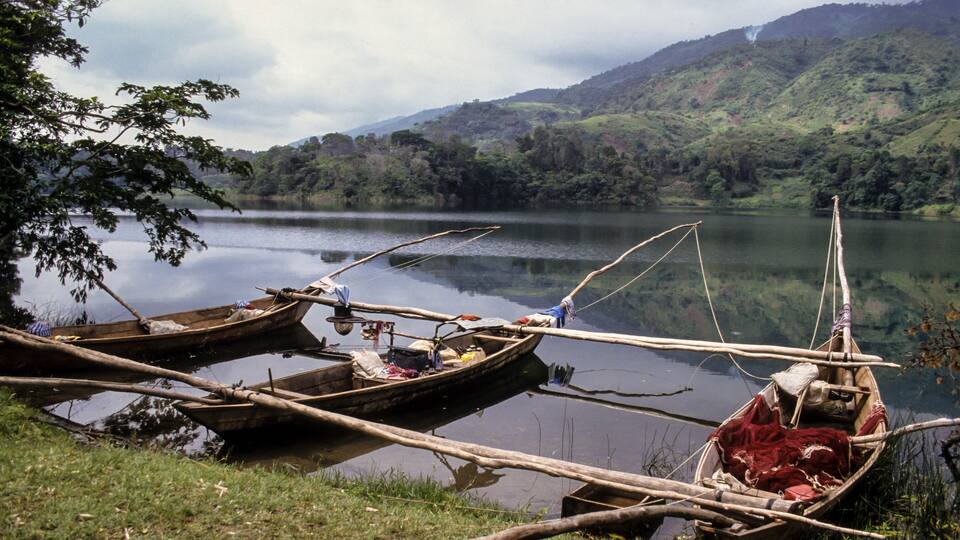 A calm lake with boats tied to the shore, surrounded by lush green hills.
