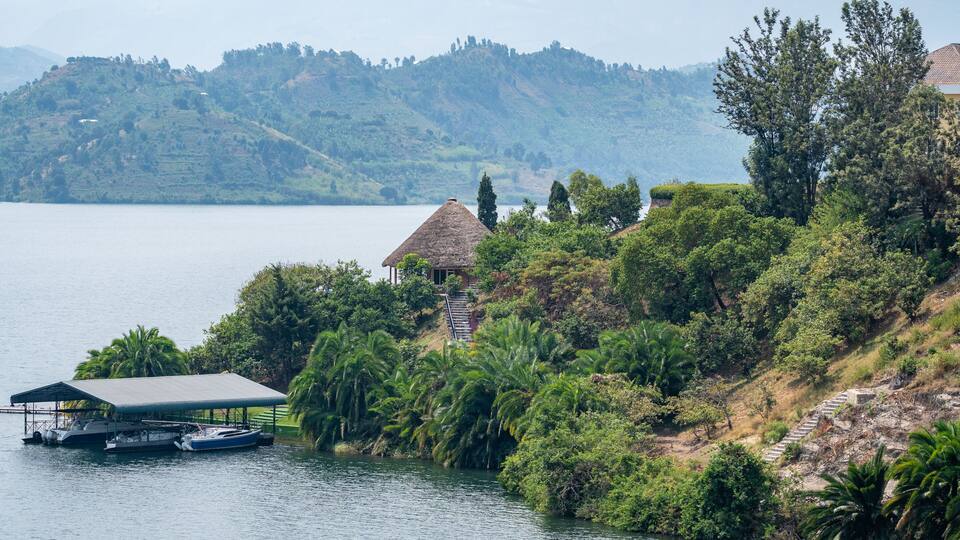 A lake with boats docked, a thatched-roof hut, and lush greenery.