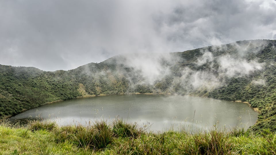 A lake surrounded by lush green hills with steam rising from the terrain.