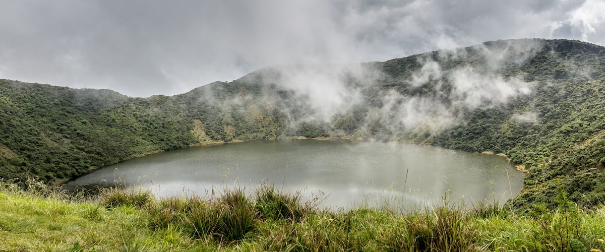 A lake surrounded by lush green hills with steam rising from the terrain.