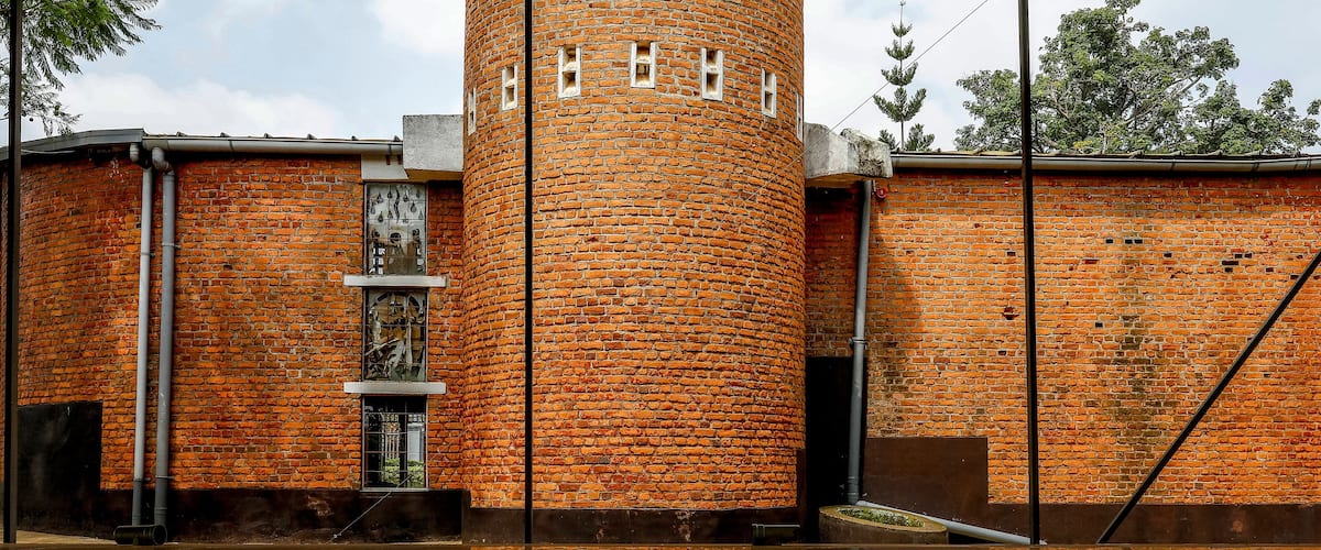 A brick tower with a reflection in a puddle, surrounded by trees and a cloudy sky.