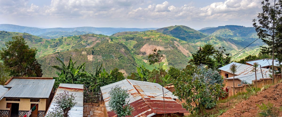 A rural landscape with terraced fields, houses with corrugated metal roofs, and rolling hills in the background.