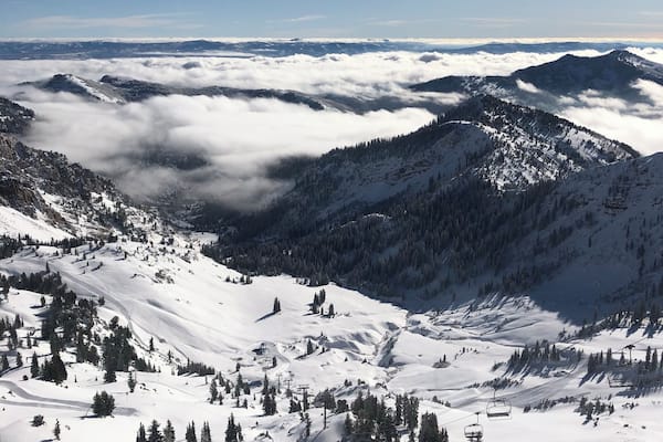 Un paysage de montagne enneigé, avec un télésiège et une vallée remplie de nuages.