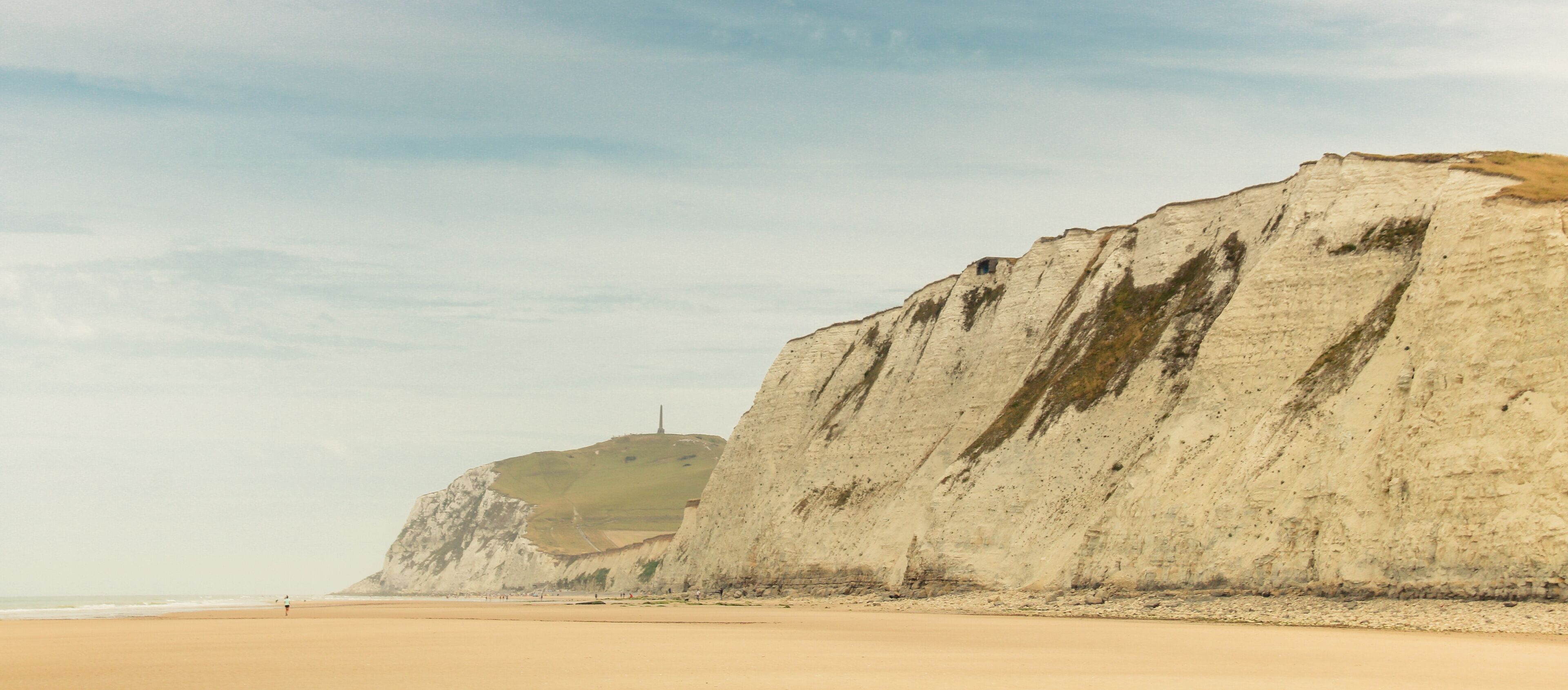 A coastal landscape with a sandy beach and prominent white cliffs.
