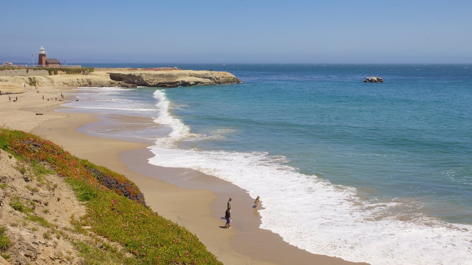 A sandy beach with waves, a lighthouse, and rocky outcrops.