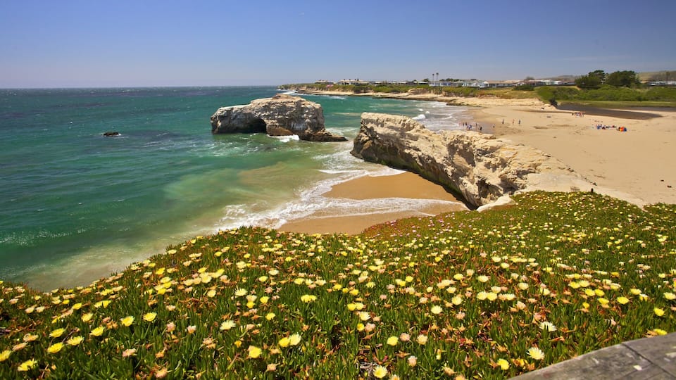 A coastal landscape with clear turquoise waters, a sandy beach, and a rocky outcrop.