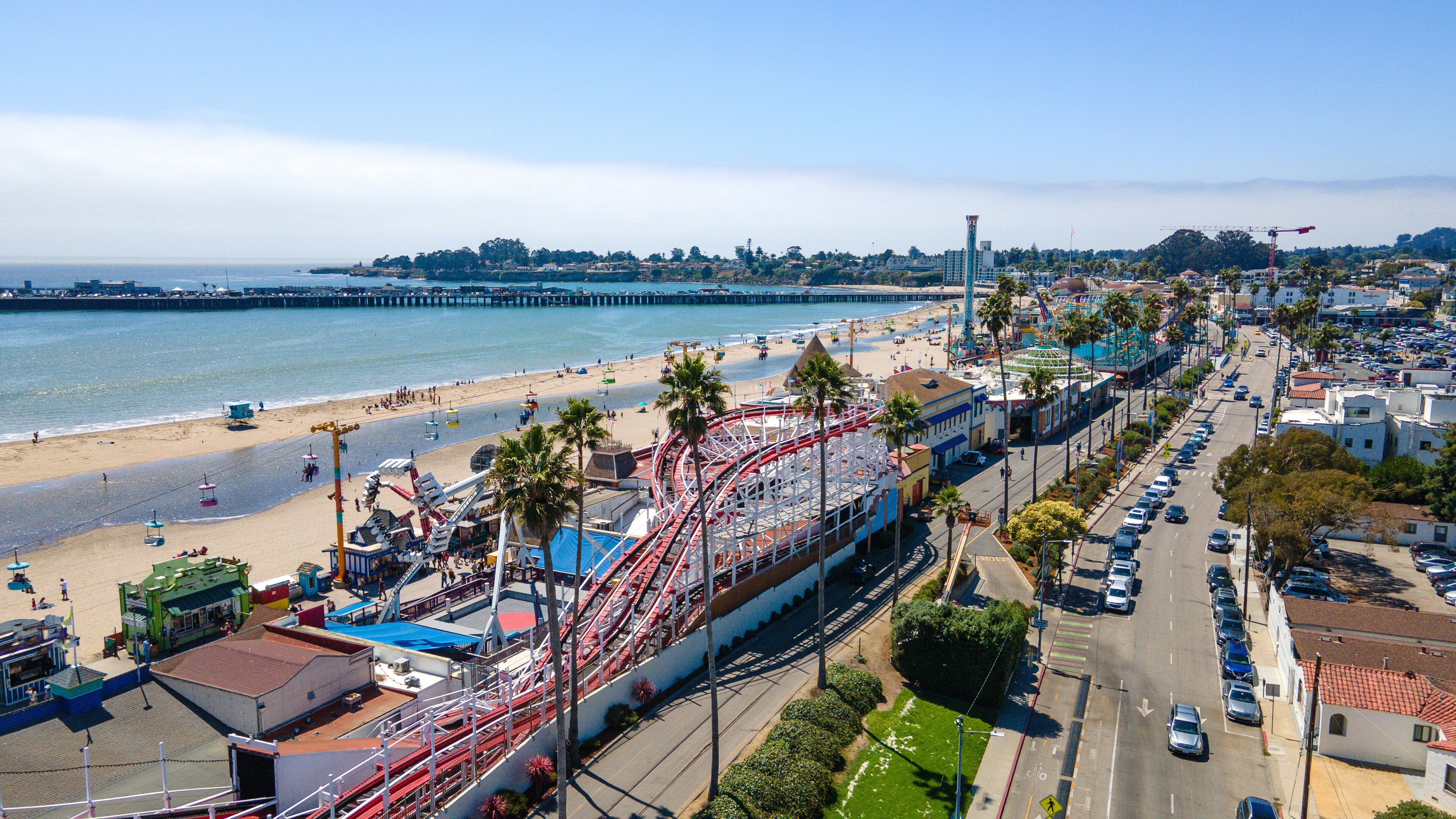 A coastal amusement park with a roller coaster, beach, and pier.