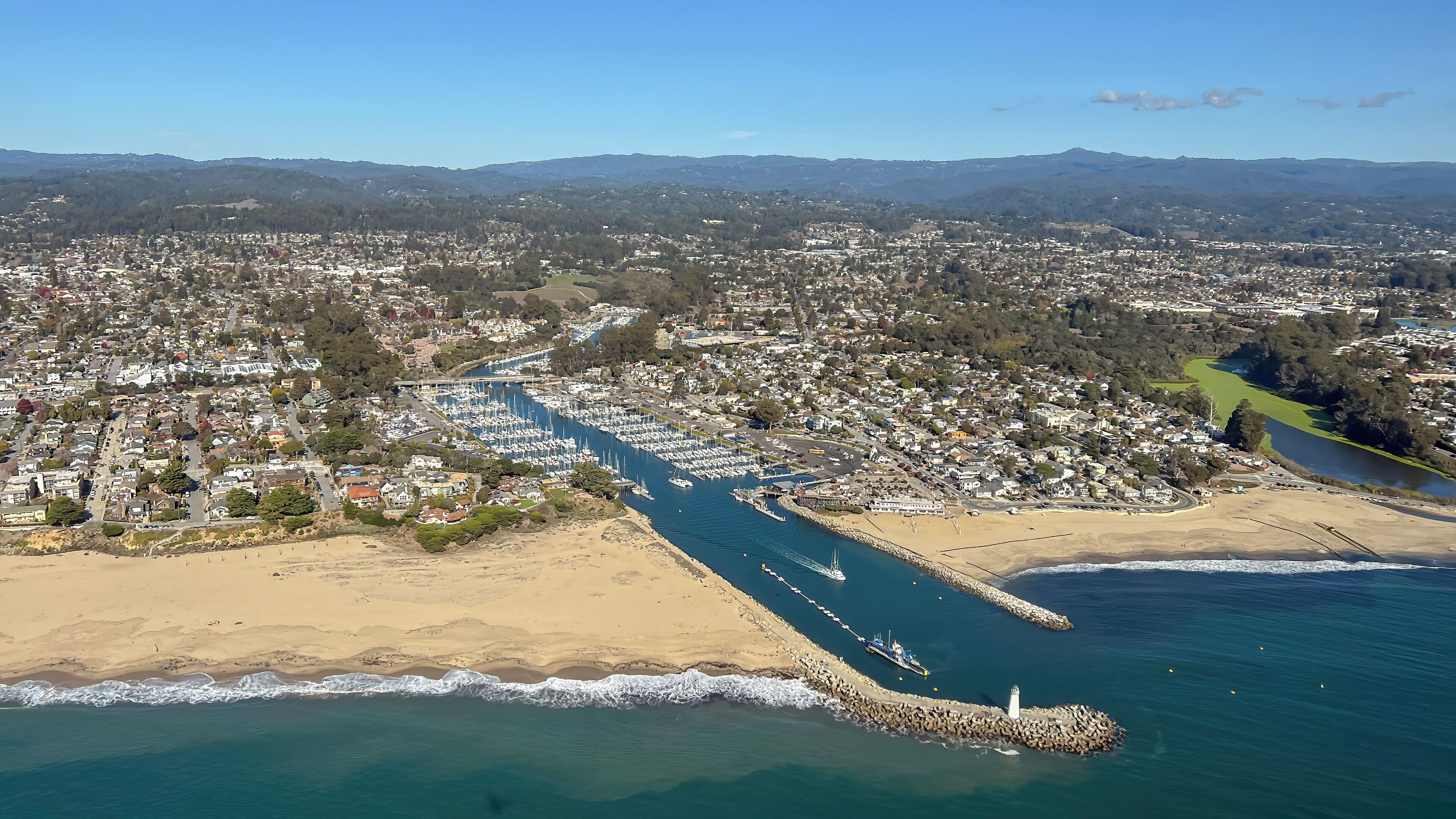 An aerial view of a coastal town with a marina, beach, and surrounding hills.