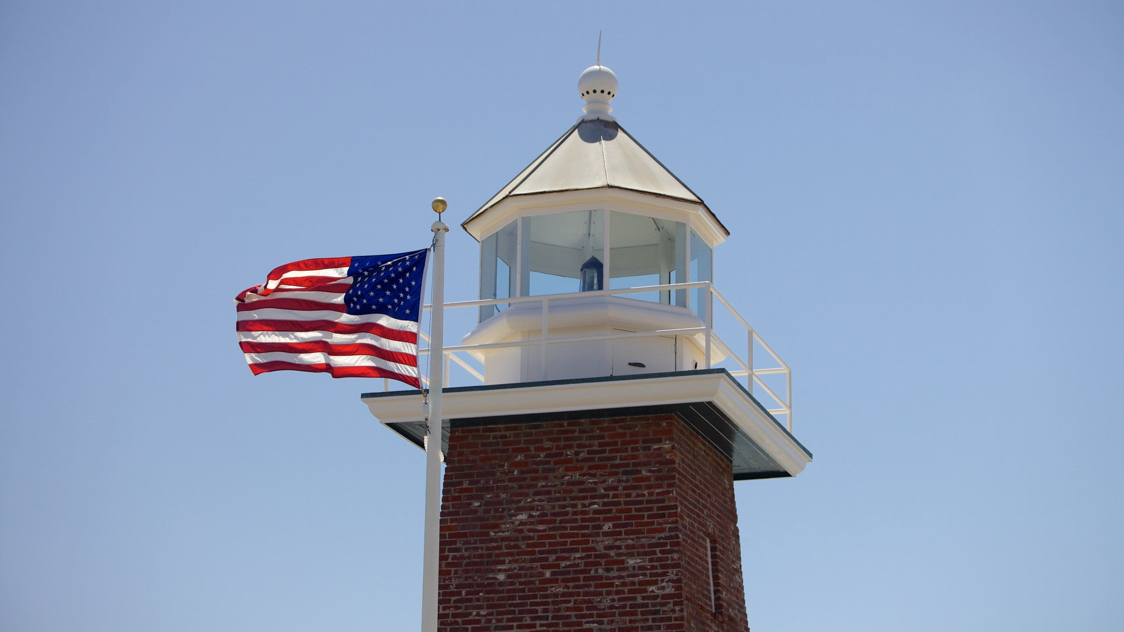 Een bakstenen vuurtoren met een witte koepel en een vlaggenmast waarop de Amerikaanse vlag wappert.