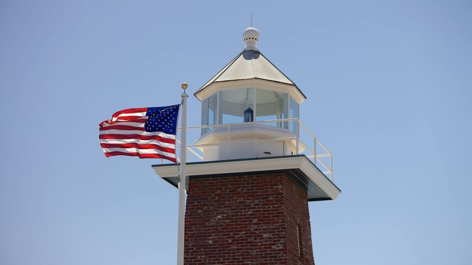 Een bakstenen vuurtoren met een witte koepel en een vlaggenmast waarop de Amerikaanse vlag wappert.