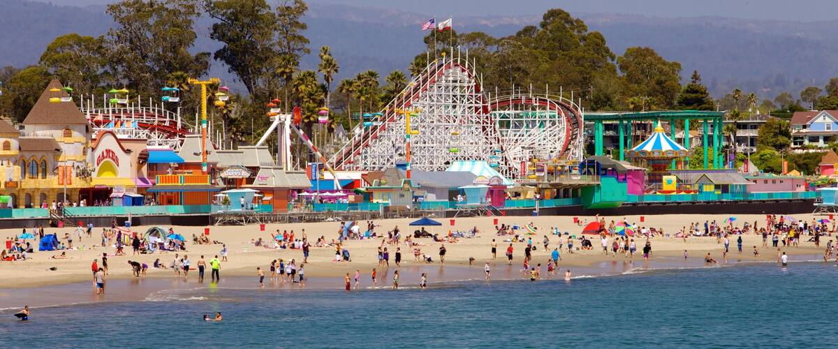 Una playa con una noria y atracciones de parque de diversiones al fondo.