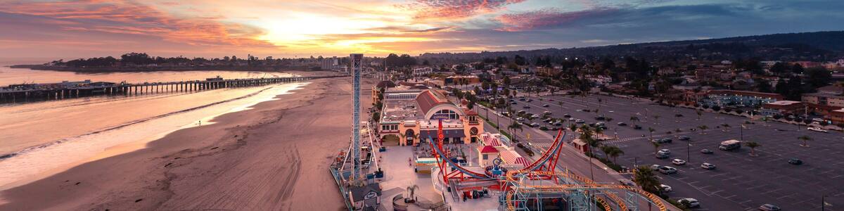 A coastal amusement park with roller coasters and a beach at sunset.