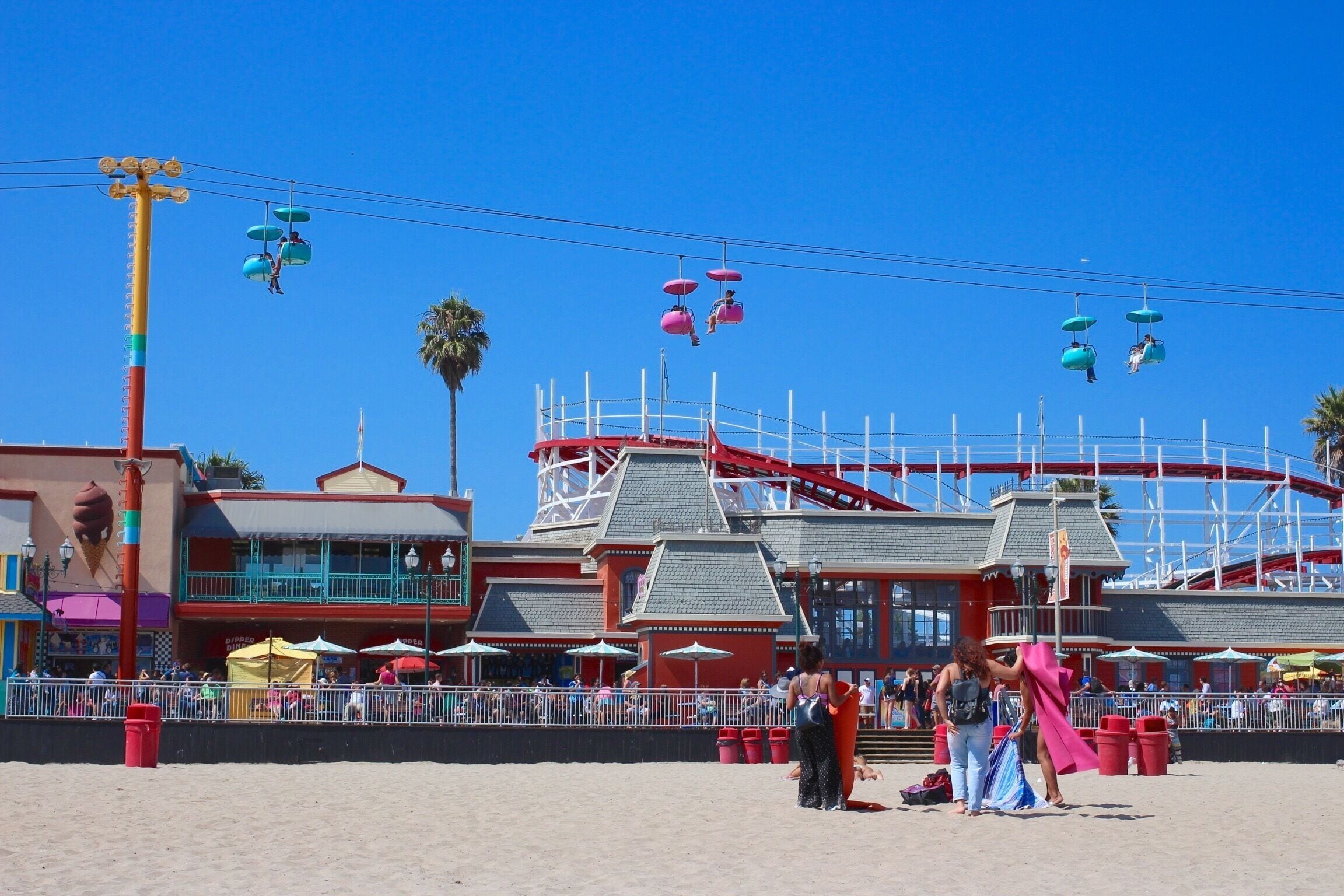 Un parc d’attractions situé en bord de mer, avec une grande roue, des montagnes russes et un bâtiment doté d’un toit rouge.