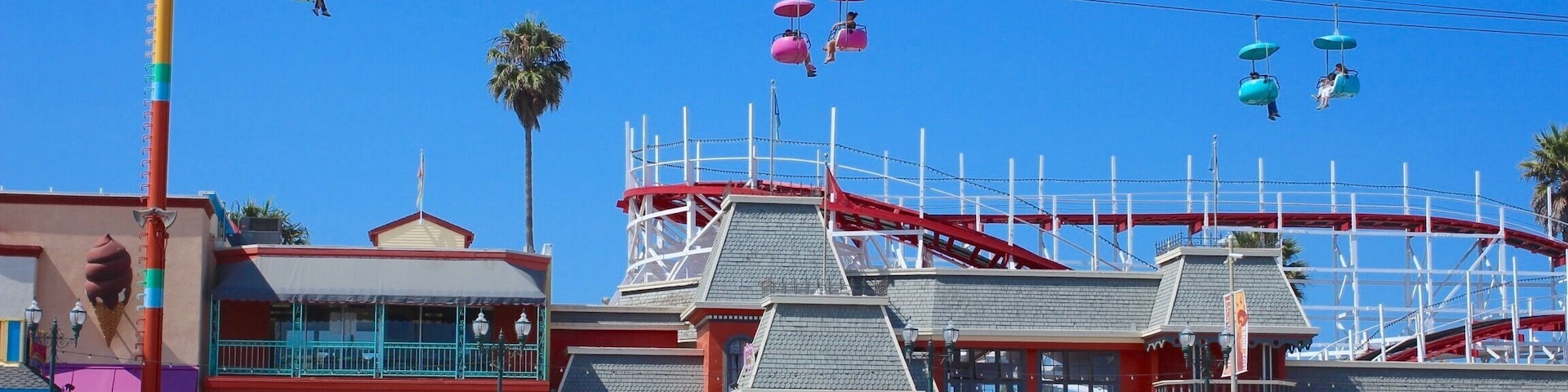 Ein Vergnügungspark direkt am Strand, mit Riesenrad, Achterbahn und einem Gebäude mit rotem Dach.