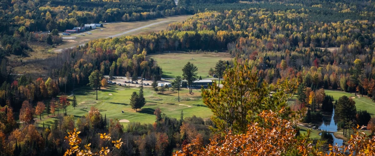A golf course surrounded by autumn-colored trees and a distant view of a hill.