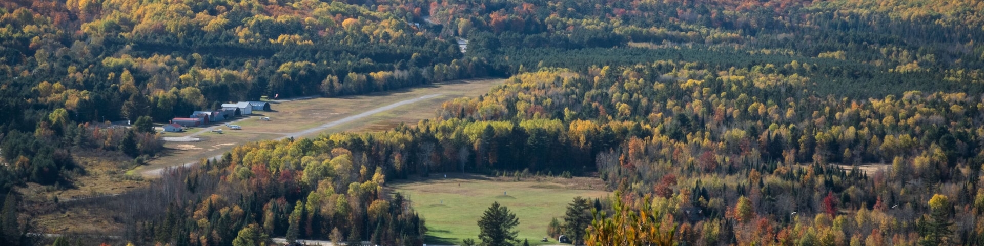 A golf course surrounded by autumn-colored trees and a distant view of a hill.