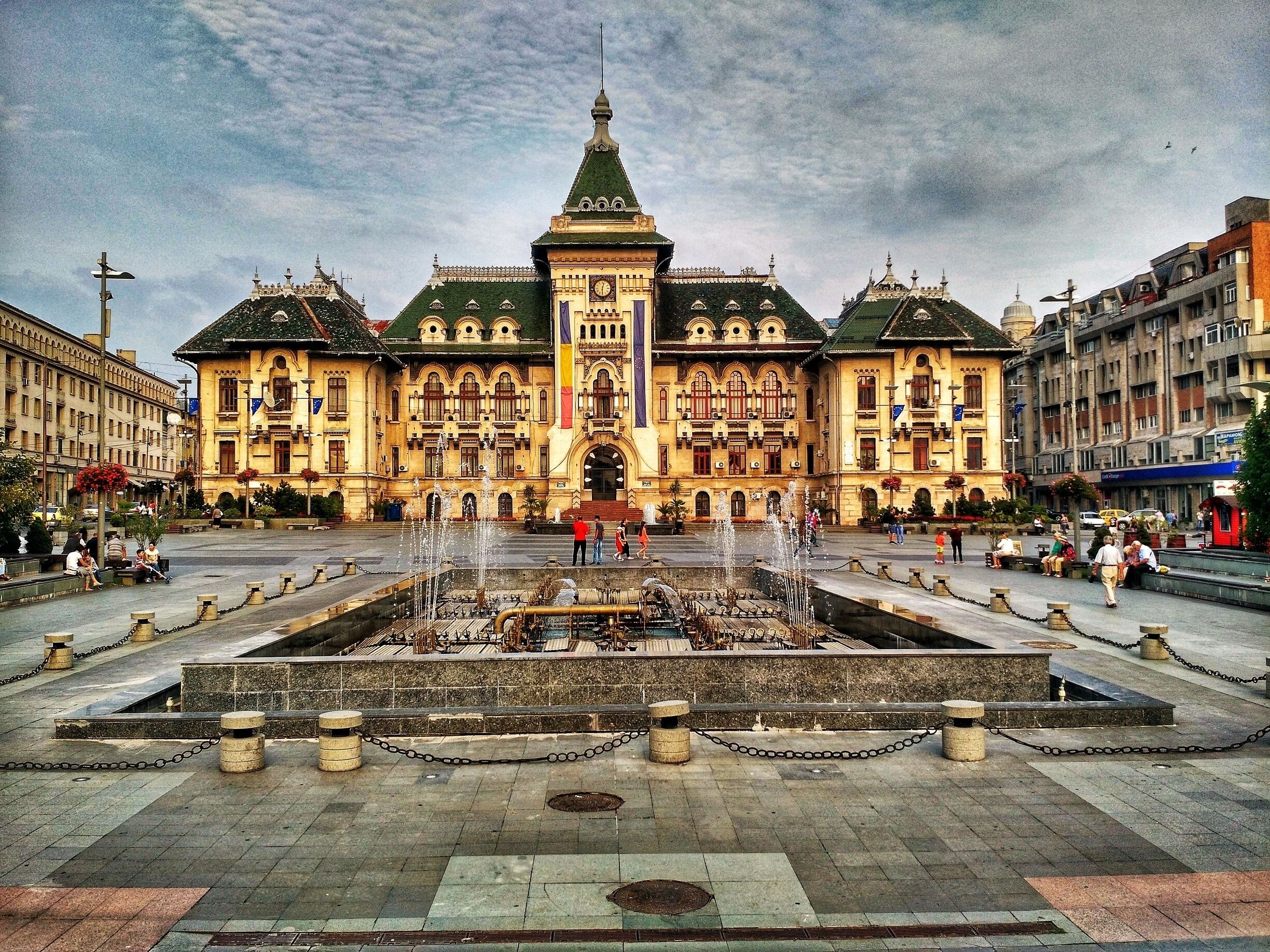 A grand building with a central fountain, surrounded by a square with stone bollards and chains.