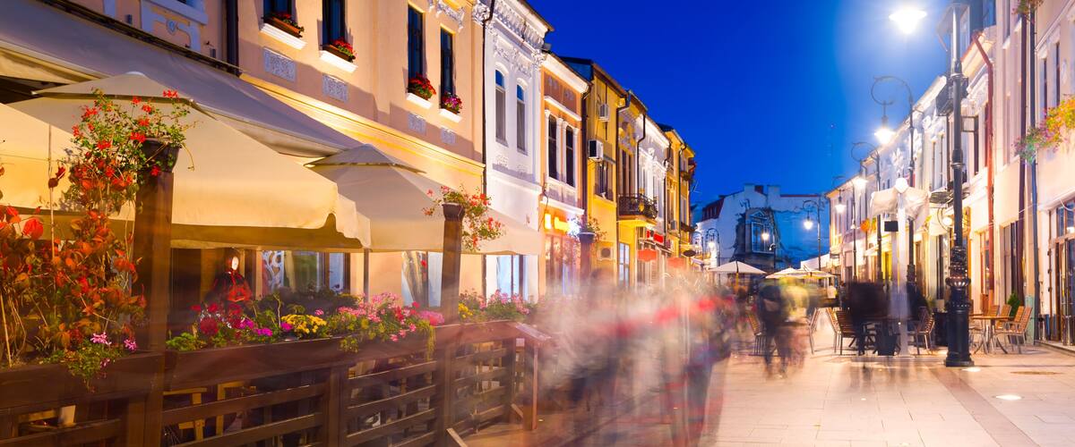 A street with buildings, outdoor seating, and a clear sky.