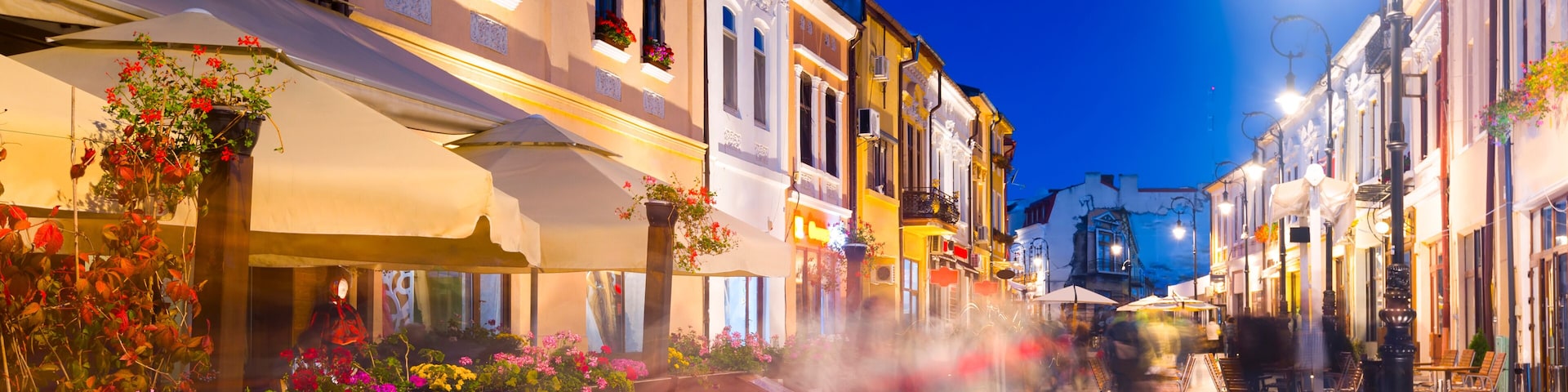 A street with buildings, outdoor seating, and a clear sky.