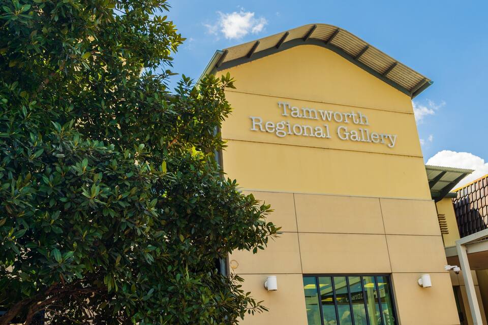 The exterior of the Tamworth Regional Gallery with a clear sky and lush green foliage.
