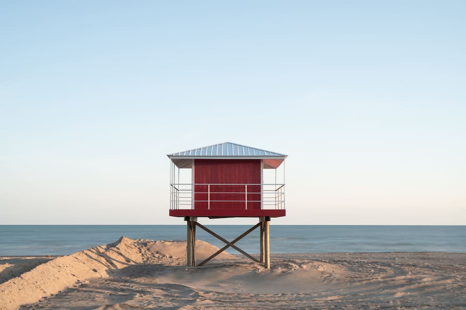 Una torre de salvavidas en una playa arenosa con el océano al fondo.
