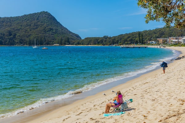 Une plage avec une montagne en arrière-plan, une personne qui pêche et une chaise de plage avec une serviette.