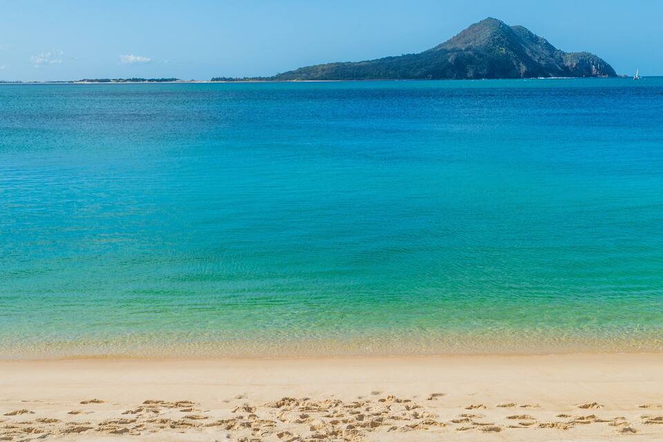 A beach with clear turquoise water, a sandy shore, and a distant island.