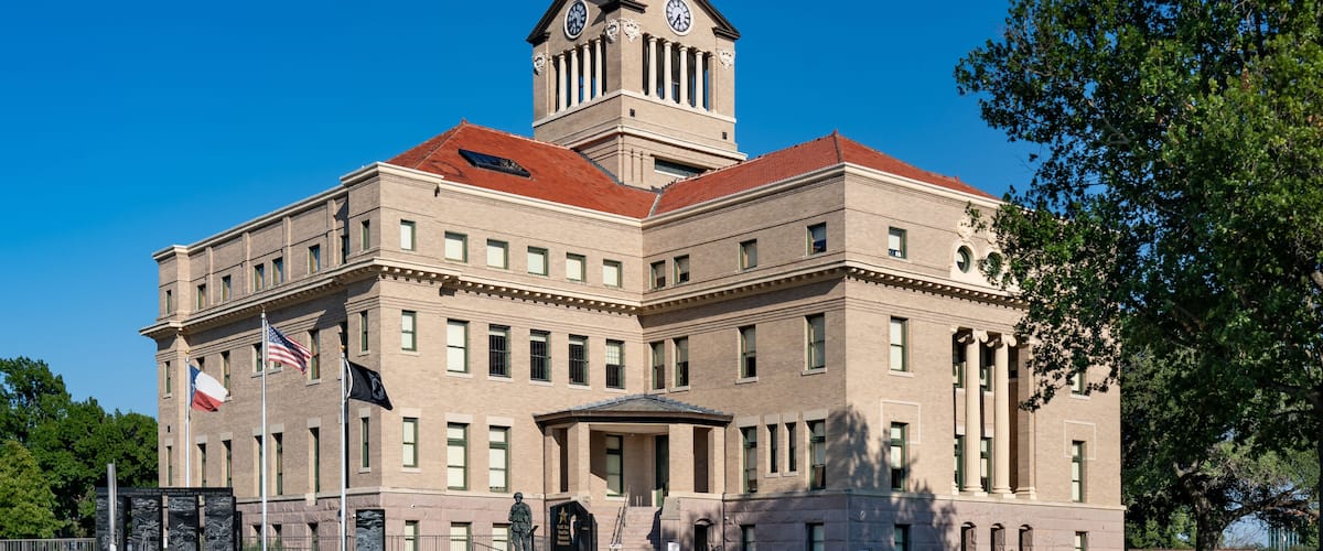 A large, historic building with a clock tower, columns, and a red roof.