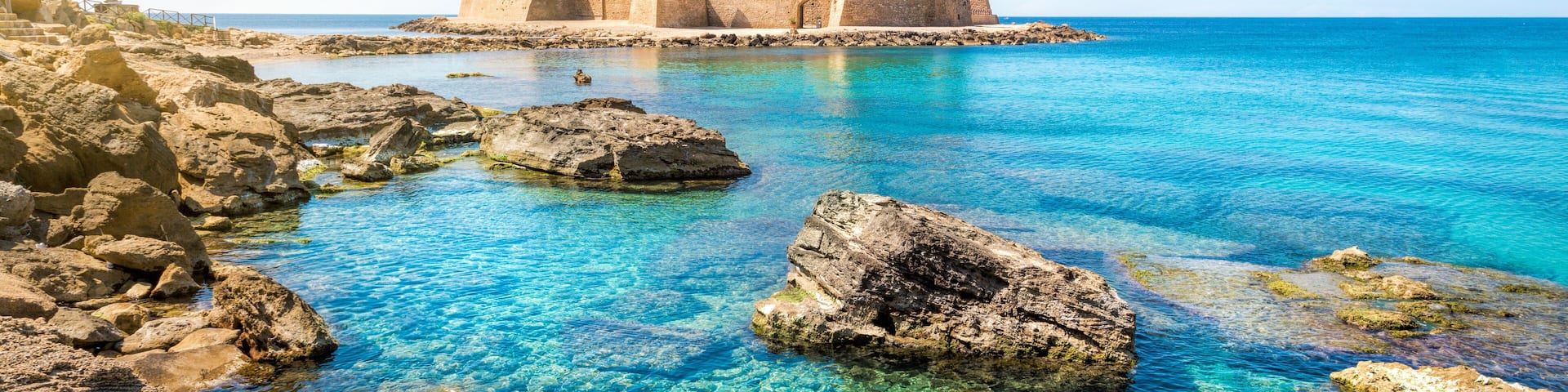 A coastal castle surrounded by clear blue waters and rocky shores.