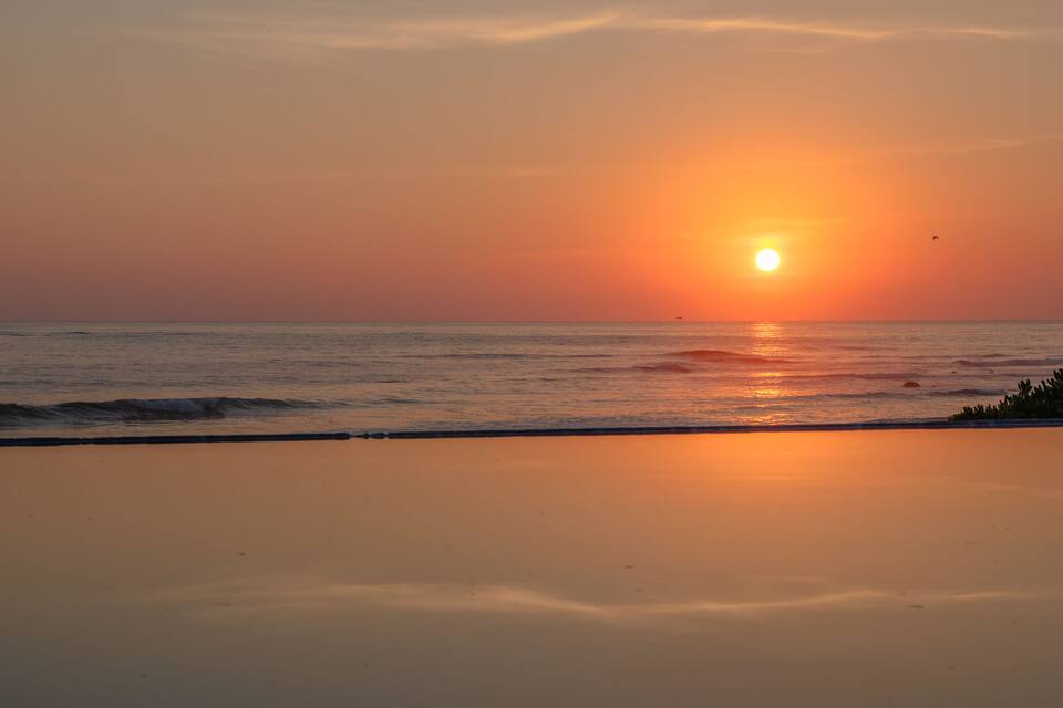 A sunset over the ocean with waves on the shore.