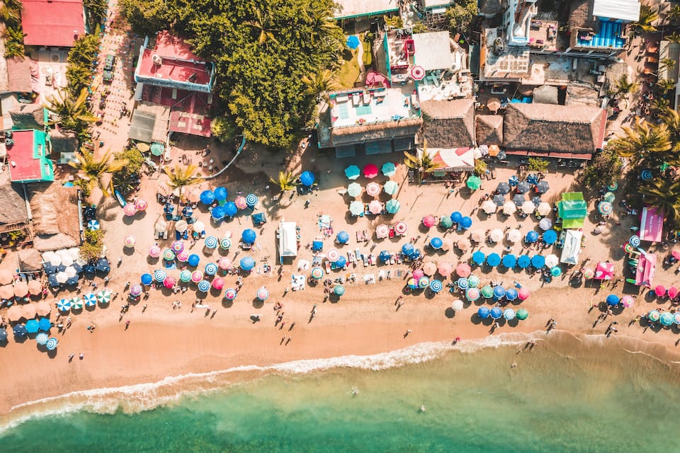 An aerial view of a beach with numerous colorful umbrellas and people.